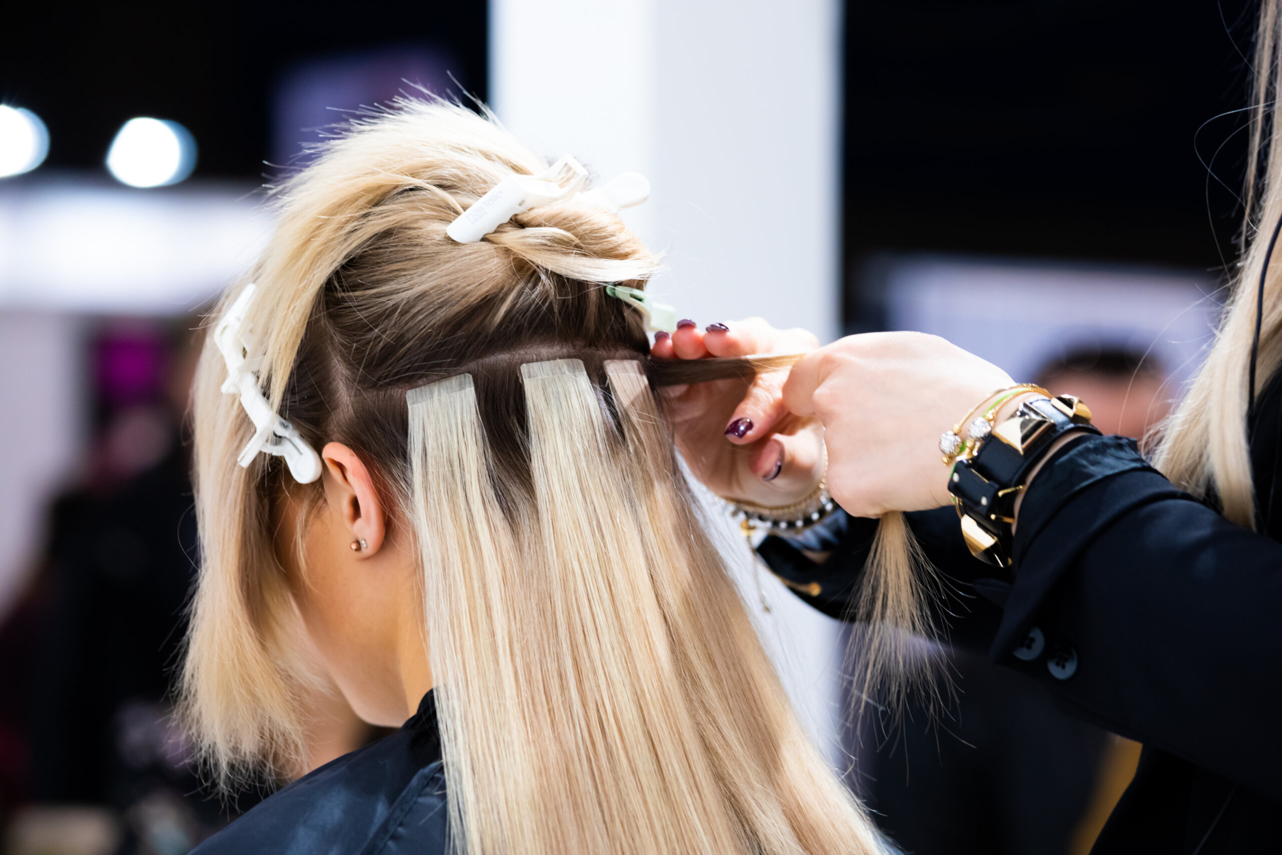 Professional hair dresser making hair extensions for blonde girl in a beauty salon