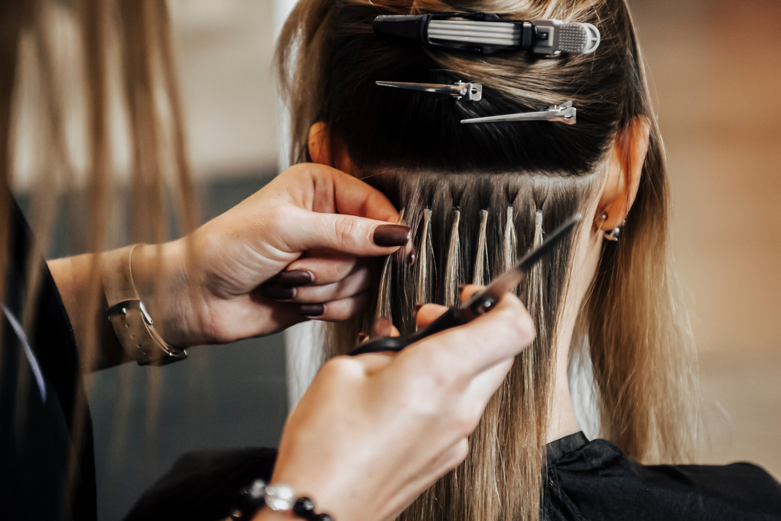The hairdresser does hair extensions to a girl, a blonde in a beauty salon. Professional hair concept